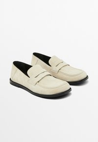 Beige suede loafers with a flat black sole, featuring a smooth toe and decorative stitching on the vamp. Simple and classic design.