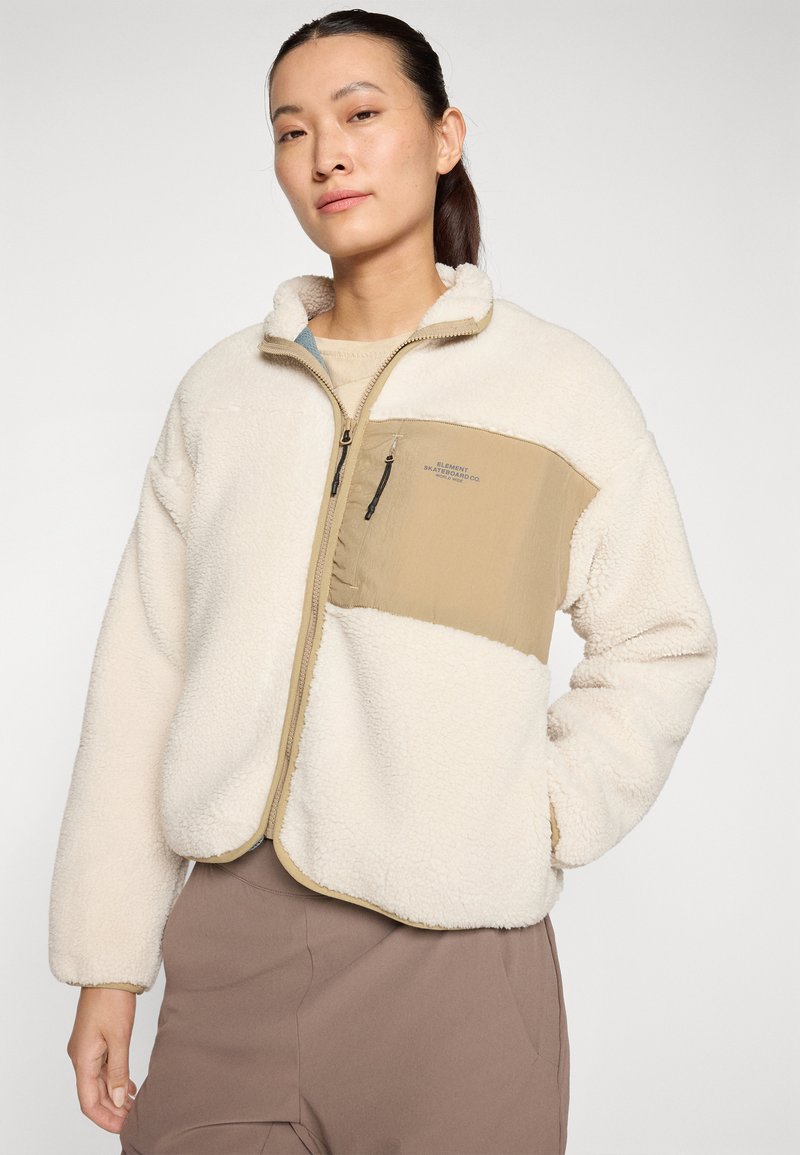 Giacca in pile di colore crema con un pannello beige, dotata di chiusura a zip e superficie texturizzata. Include una piccola tasca con zip sul petto.