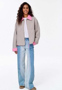 Šedá bunda s růžovým límcem, spárovaná s světle modrými rozšiřujícími se džíny. Bunda má zipové zapínání a kontrastní růžové manžety.