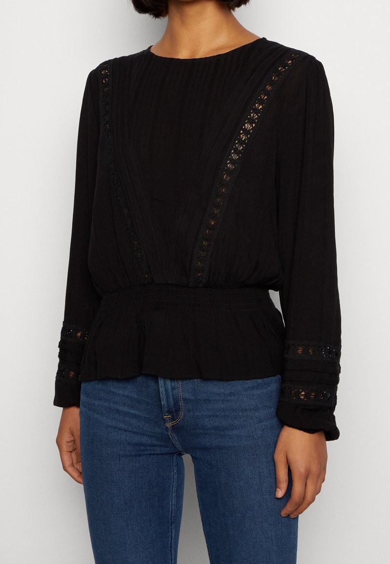 Musta pitkähiainen paita, jossa on teksturoitu kangas, pitsiyksityiskohtia kaula-aukossa ja hihoissa, kootut vyötärölinjat sekä rento malli.