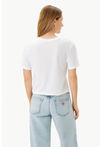 T-shirt bianco croppato con maniche corte, design semplice, texture morbida e vestibilità comoda, abbinato a jeans in denim blu chiaro con tasche.