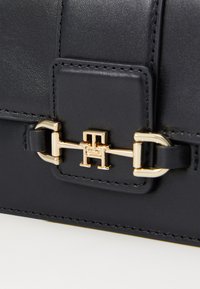 Borsa a tracolla in pelle nera con chiusura in metallo color oro, texture liscia e cuciture precise lungo i bordi.