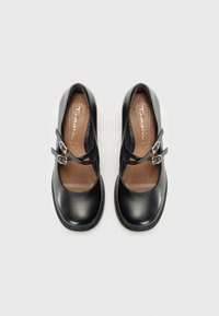 Black leather shoes with a rounded toe, featuring two black straps with silver buckles. Brown cushioned insole with perforations for breathability.