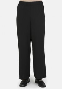 Pantalon noir ample avec taille élastique, présentant une texture lisse et un design à jambes droites. Porté avec des chaussures noires.