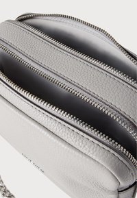 Γκρι δερμάτινη τσάντα χιαστί με τρεις θήκες με φερμουάρ, υφή εξωτερικού μέρους και ασημένιες λεπτομέρειες. Ανθεκτικός και κομψός σχεδιασμός.