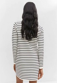 Abito in maglia con maniche lunghe, presenta strisce orizzontali nere su fondo bianco, lunghezza fino a metà coscia e scollatura rotonda.