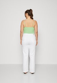 Top verde sin mangas con tirantes finos, combinado con pantalones blancos de tiro alto y de pierna ancha. El conjunto presenta una textura suave y un diseño minimalista.