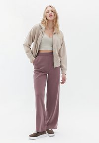 Beige Zip-Jacke, hellgrünes Crop-Top und weite mauve Sweatpants. Braune Sneaker mit weißen Sohlen. Weiche, lässige Stoffstrukturen.