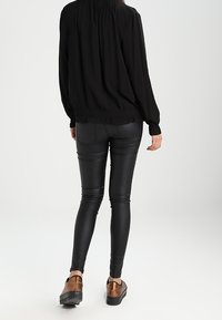 Svart långärmad blus med rynkad krage, kombinerad med figurnära svarta faux-läder leggings och bruna slip-on skor.