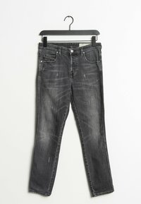 Jeans slim fit de color negro con un ligero desgaste colgando de una percha negra sobre un fondo blanco.