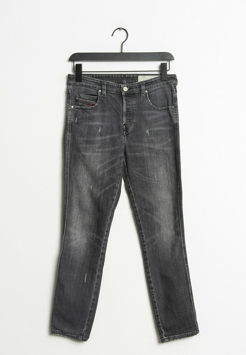 Jeans slim fit de color negro con un ligero desgaste colgando de una percha negra sobre un fondo blanco.