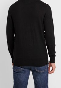 Black knit sweater with long sleeves, ribbed cuffs and hem. Worn with blue denim jeans, textured fabric visible on pants.