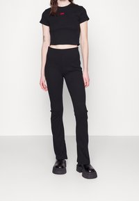 Zwarte cropped t-shirt met korte mouwen en een rood logo, gecombineerd met zwarte slim-fit broek. Beide gemaakt van een gladde, rekbare stof.