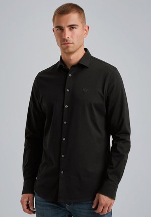 Camisa de manga larga negra con cuello, que presenta botones y un pequeño logo. Textura suave, corte entallado y diseño de dobladillo recto.