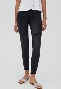 Mustat skinny-farkut, joissa on repeytymät polvissa, korkealla vyötäröllä, hieman rispaantuneilla lahkeensuilla ja sileällä, joustavalla materiaalilla.