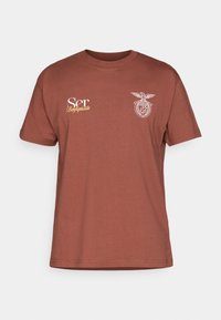 Ρουμπινί κοντομάνικο T-shirt με λευκή και κίτρινη επιγραφή "Ser Benfiquista" και λευκό λογότυπο με αετό στο στήθος.