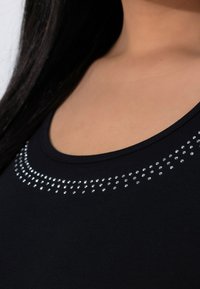 Black tank top featuring a round neckline, embellished with a row of small, silver rhinestones arranged in a slight arc.