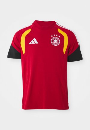 Czerwona koszulka narodowej drużyny piłkarskiej Niemiec z czarnymi rękawami, żółtymi akcentami na ramionach, logo Adidasa oraz herb zespołu z czterema gwiazdami na piersi.