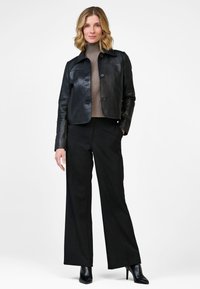 Black leather cropped jacket with a collar and button closure, paired with a brown turtleneck and black wide-leg trousers. Heeled shoes.