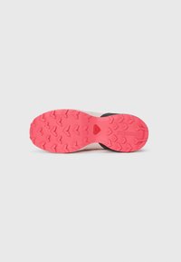 Semelle de chaussure de trail avec une surface en caoutchouc rose texturé, présentant des crampons dessinés pour une traction et une section noire lisse près du talon.