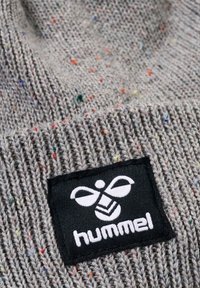 Grijze gebreide beanie met veelkleurige spikkels, voorzien van een zwart label met een wit bijlogo en het merknaam "hummel" aan de voorkant.