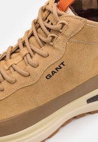 Tanfarbene Wildledersneaker mit beigen Akzenten, runden Schnürsenkeln, Gummisohle und schwarzem "GANT"-Logo an der Seite. Verfügt über ein strukturiertes Obermaterial für besseren Halt.