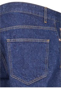 Jeans de mezclilla azul oscuro con un solo bolsillo trasero, costuras doradas y una cinturilla ajustada con pasadores para cinturón.
