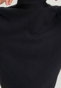 Svart polotröja i slät trikåmaterial. Har hög krage och en figurnära design med långa ärmar.