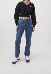 Svart kort sweatshirt med V-hals, kombinerad med blå raka jeans och svart-vita sportskor med en swoosh-logotyp.