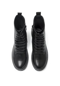 Botas de tobillo de cuero negro con cordones en la parte delantera y cremallera lateral. Presentan un acabado suave y costuras blancas a lo largo de la suela.