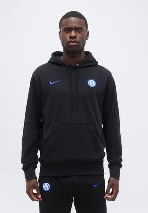 Άνδρας με μαύρο φούτερ και παντελόνι Nike με μπλε λογότυπα του ποδοσφαιρικού συλλόγου Ίντερ Μιλάνο, στέκεται μπροστά σε απλό λευκό φόντο.
