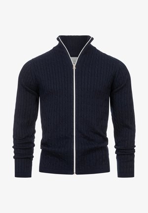 Marinblå kabelstickad cardigan med ribbad krage, hel dragkedja och långa ärmar. Har mjuk textur och kontrasterande vit dragkedja.