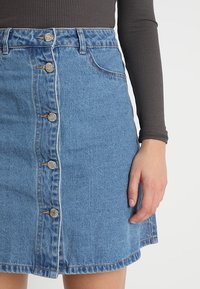 Blaue Denim-A-Linien-Rock mit einer Knopfleiste und fünf Metallknöpfen, mit einem ausgefransten Saum und einem leichten Verblassen für einen lässigen Look.