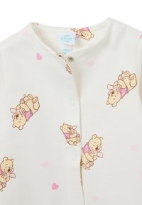 Weißer Baby-Overall mit pastellrosa Herzen und einem wiederholten Cartoon-Muster von Winnie Puuh, der ein kleines Kaninchen hält, mit Druckknöpfen.