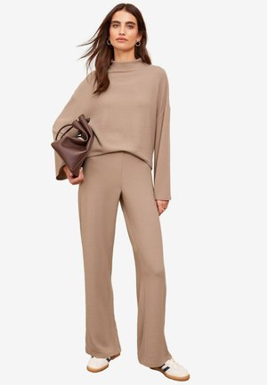 Beige knit sweater with high neckline and wide sleeves, paired with matching wide-leg pants. Brown bag in hand, white and black sneakers.