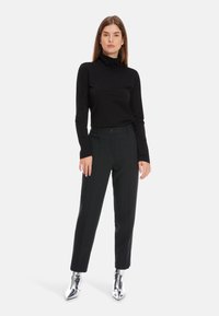 Schwarzes Langarm-Rollkragenoberteil, kombiniert mit maßgeschneiderten schwarzen Hosen; silberne spitze Ankle-Boots sorgen für ein reflektierendes Detail.