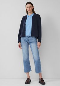 Modra zip-up jakna preko svetlo modrega polo majice, v kombinaciji s svetlo modrimi ravnimi kavbojkami in temno rjavimi platformskimi loaferji. Preprost dizajn.