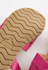 Sandal in pelle rosa con suola in gomma marrone texturizzata caratterizzata da un motivo a ondulazione e logo in rilievo. Il design delle cinghie consente un'esposizione aperta del piede.