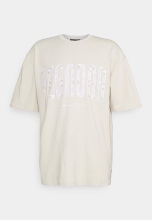 Camiseta de corte oversized en color beige, con mangas cortas y un gran texto estampado "PEGADOR" en el pecho. Justo debajo, un texto más pequeño que dice "Atlantic Peace."