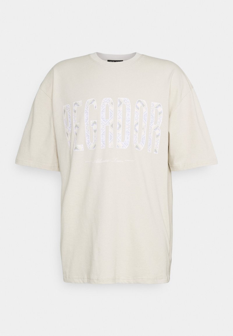 Beige oversized T-shirt med korta ärmar och stor mönstrad text "PEGADOR" över bröstet, med mindre text nedanför som lyder "Atlantic Peace."