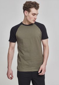 Olivovo zelené tričko s čiernymi raglanovými rukávmi, vyrobené z bavlny. Krátke rukávy, crew neck, hladká textúra, priliehavý strih bez viditeľných vzorov.