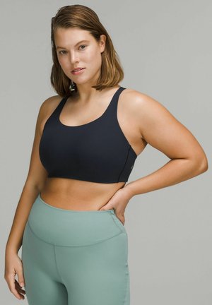 Black sports bra with wide straps and a scoop neckline, paired with high-waisted, mint green leggings, featuring a smooth texture.