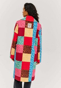 Farebné patchworkové sako so živými štvorcami v červenej, modrej, ružovej, žltej, zelenej a hnedej leopardiej potlači, s špicatým golierom a predným štítkom.