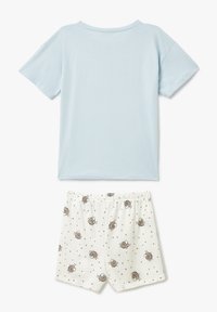 Camiseta de algodón azul claro con cuello redondo y mangas cortas, combinada con pantalones cortos blancos que presentan un patrón de erizos y puntos dorados.