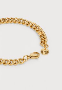 Goldfarbener Kettenarmband mit großen Gliedern, Karabinerverschluss und einem runden Anhänger mit einem gravierten Logo auf weißem Hintergrund.