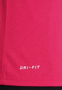 Rosa träningskortärmad tröja i fukttransporterande tyg, med rundade sidsömmar, sömnadsdetaljer och en vit "DRI-FIT" logotyp på nedre sidan.