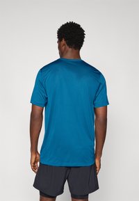 Kortærmet t-shirt med rund hals i ensfarvet teal stof. Har en glat tekstur og afslappet pasform, kombineret med mørke shorts.
