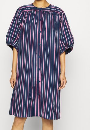 Robe bleu marine avec des rayures verticales roses et blanches, boutons sur le devant et manches bouffantes jusqu'au coude, portée par une personne debout.