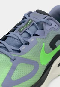 Το αθλητικό παπούτσι διαθέτει ελαφρύ επάνω μέρος από δίχτυ σε πράσινο και μοβ, με εμφανές πράσινο λογότυπο Nike και δομικές λεπτομέρειες σε μαύρο.