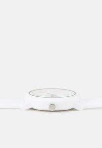 Reloj de pulsera blanco con un diseño redondo, dial claro, acentos verdes, manecillas rojas y una correa de silicona texturizada con un botón lateral plateado.